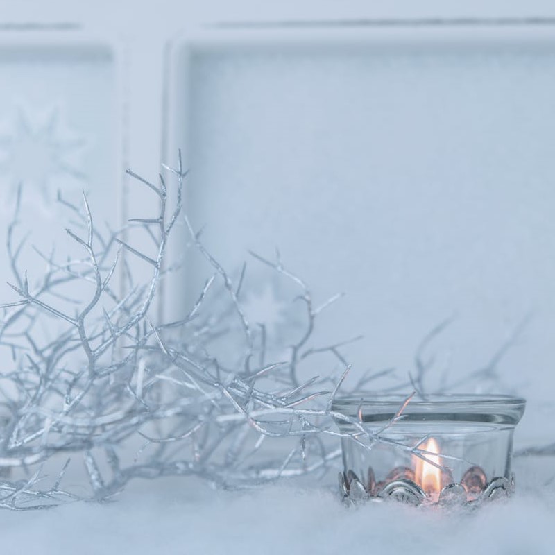 weisser-zweig-teelicht-im-glas-im -schnee-vor-weisser-scheibe